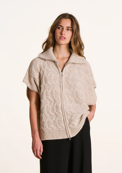 Femme portant un gilet oversize torsadé écru à manches courtes tombantes, col camionneur et fermeture zippée.
Ref. FK-GI-ELISE-C_266 – La Fée Maraboutée