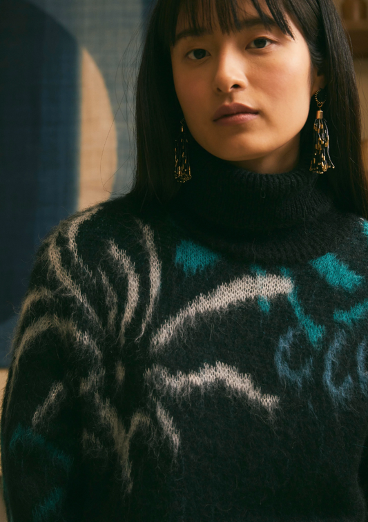Gros plan d’un pull noir en jacquard végétal avec col roulé, porté par un mannequin, mettant en avant la texture mohair et les motifs bleus et ivoire.
FK-PU-EZEPICE_1503 La Fée Maraboutée